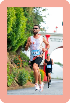 Un coureur de marathon, portant un dossard, court dans une rue de la ville lors d'une course sur route, avec d'autres participants en arrière-plan.