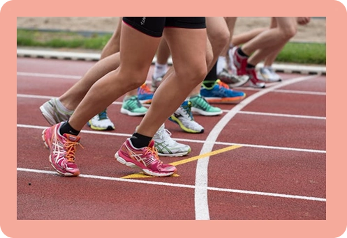 Gros plan sur les jambes de coureurs sur la ligne de départ d'une piste d'athlétisme rouge, chaussés de souliers de course colorés et se préparant à sprinter.